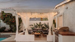 Un patio techado al aire libre con una parrilla, zona de estar y piscina.