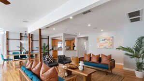 Un salón espacioso con un conjunto de sofá de madera, una mesa de comedor con sillas y una cocina al fondo.