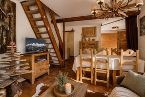 Quarto rústico com escada de madeira, cama, mesa de madeira com vela e televisão em um armário de madeira.