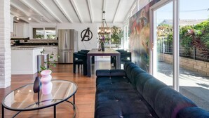 A modern kitchen with white cabinets, a stainless steel refrigerator, and a dining area with a black sofa and a glass coffee table.
