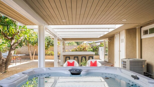 A covered outdoor hot tub area with seating and a barbecue setup.