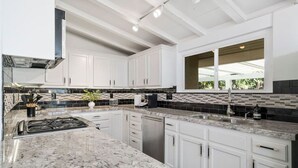 A modern kitchen with white cabinets, granite countertops, and a large window providing natural light.