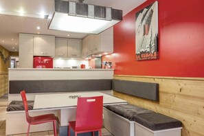 Ein moderner Essbereich mit einem weißen Tisch und roten Stühlen, im Hintergrund eine Küche und eine rote Wand mit einem Poster.