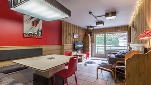 A cozy room with a dining table, red chairs, a sofa, and a TV.