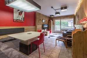 Ein gemütliches Zimmer mit Esstisch, roten Stühlen, einer Couch und einem Fernseher.
