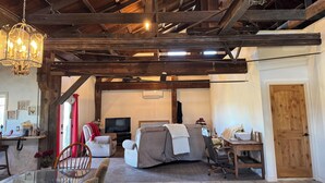 Un intérieur rustique avec des poutres apparentes, un lustre, un téléviseur et un coin salon confortable avec un canapé et des fauteuils.