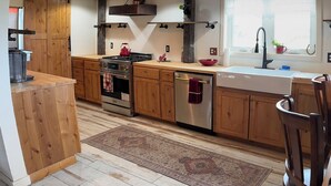 Une cuisine avec des meubles de rangement en bois, une cuisinière, un évier et des luminaires suspendus.