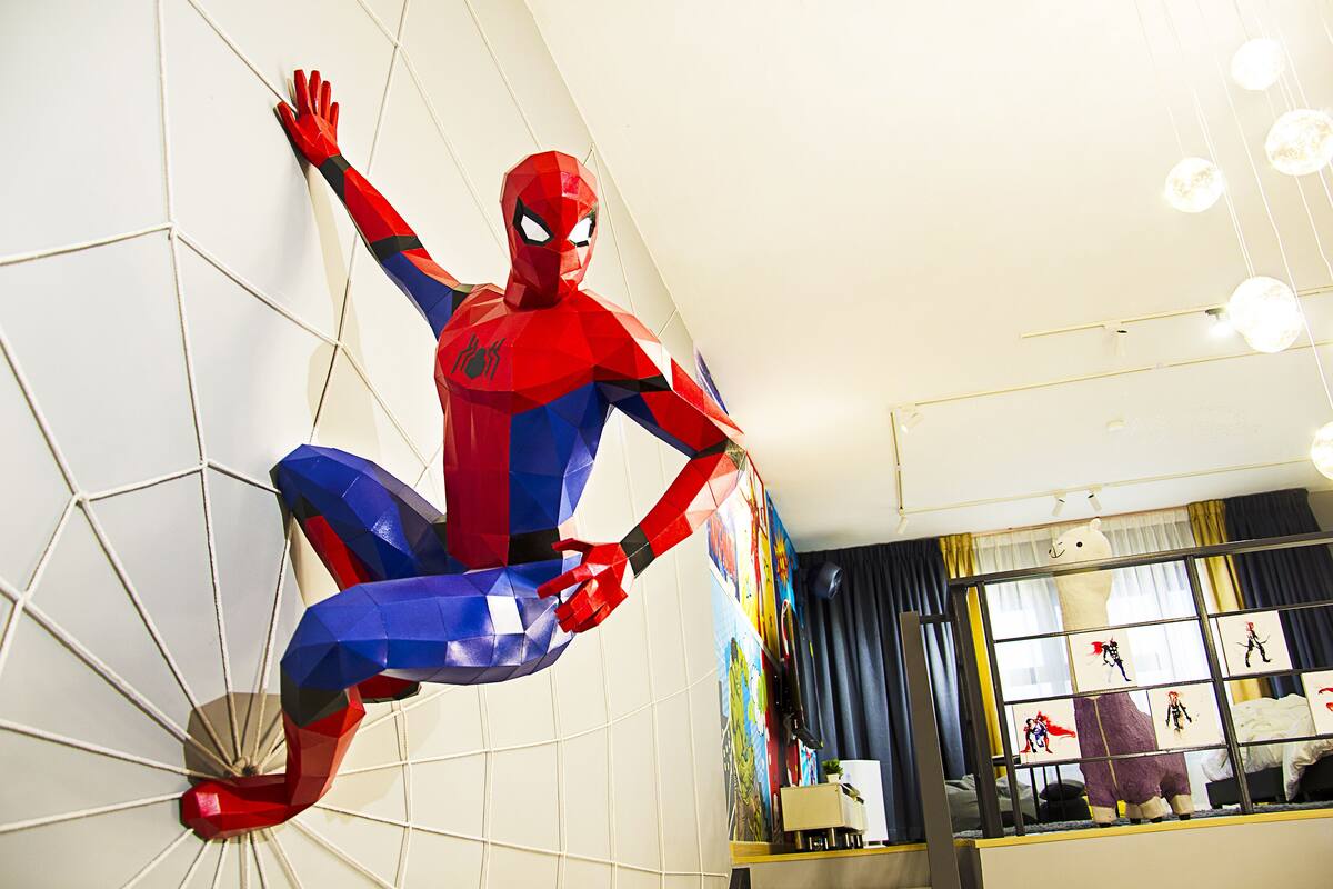 A Spider-Man statue in a room with a large window, a bed, and a wall with pictures.