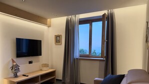 Een moderne woonkamer met een flatscreen televisie aan de muur, een houten bankje, een sofa en een raam met gordijnen.