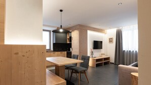 Een moderne woonkamer met een houten eettafel, grijs gestoffeerde stoelen, een grijze bank en een aan de muur bevestigde televisie.