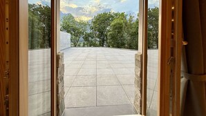Uitzicht vanaf een balkon met een stenen vloer, dat uitkomt op een stenen muur en bomen in de verte.