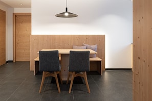 A modern dining area with a wooden table and two chairs, a bench with cushions, and a pendant light.