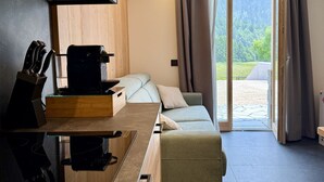 Une cuisine moderne équipée d’une cuisinière intégrée, d’une machine à café et d’un plan de travail en bois. On y trouve également un canapé et une porte-fenêtre coulissante donnant sur un balcon avec vue sur la verdure.