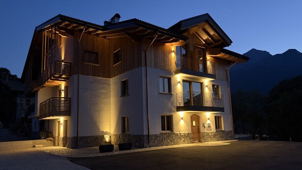 Une maison en bois à deux étages, dotée de balcons, de fondations en pierre et d’une allée.