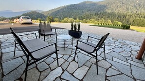 Une terrasse avec un sol en pierre, des sièges d’extérieur et une vue sur une montagne boisée.