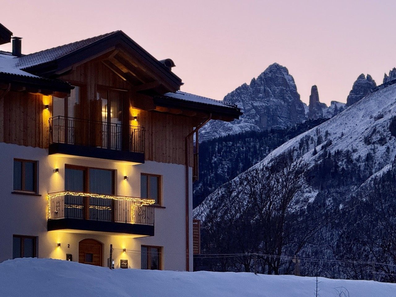 A multi-story wooden building with balconies, set against a snowy mountainous backdrop.