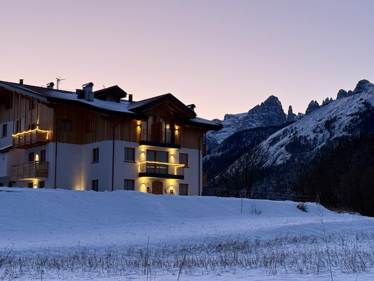 A multi-story wooden building with balconies, set against a snowy mountain backdrop.