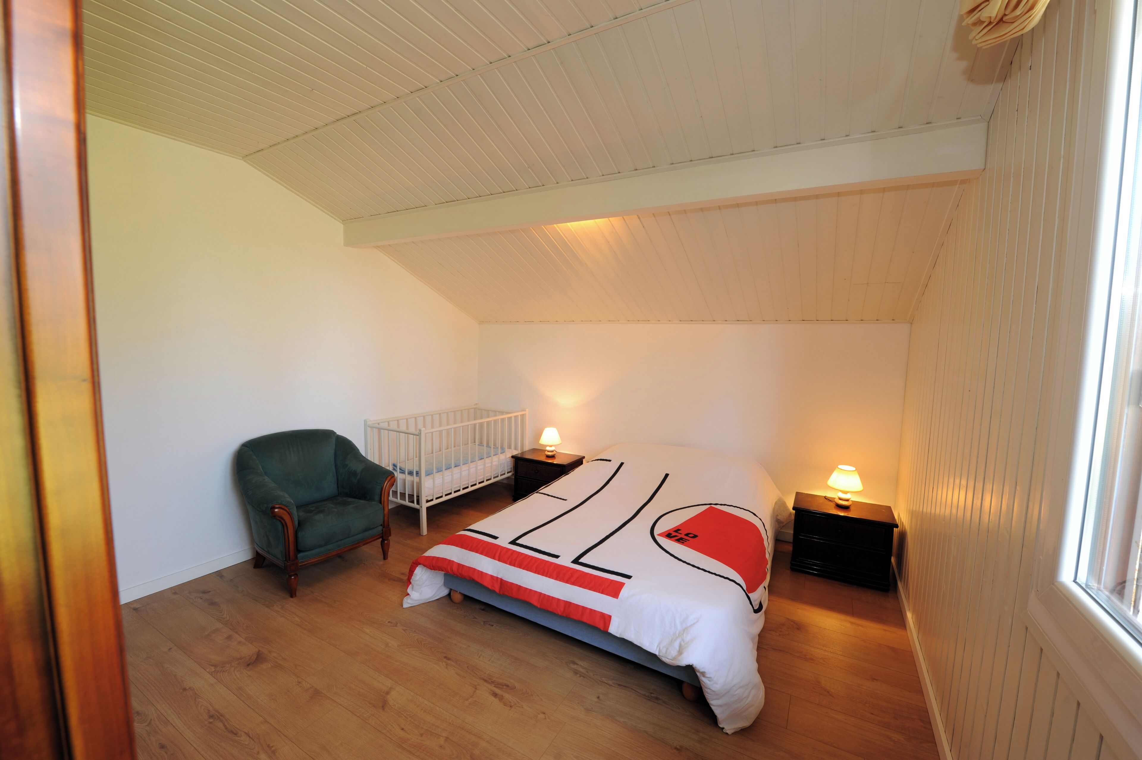 Une chambre à coucher comprenant un lit, un berceau, une chaise et deux tables de chevet avec des lampes.