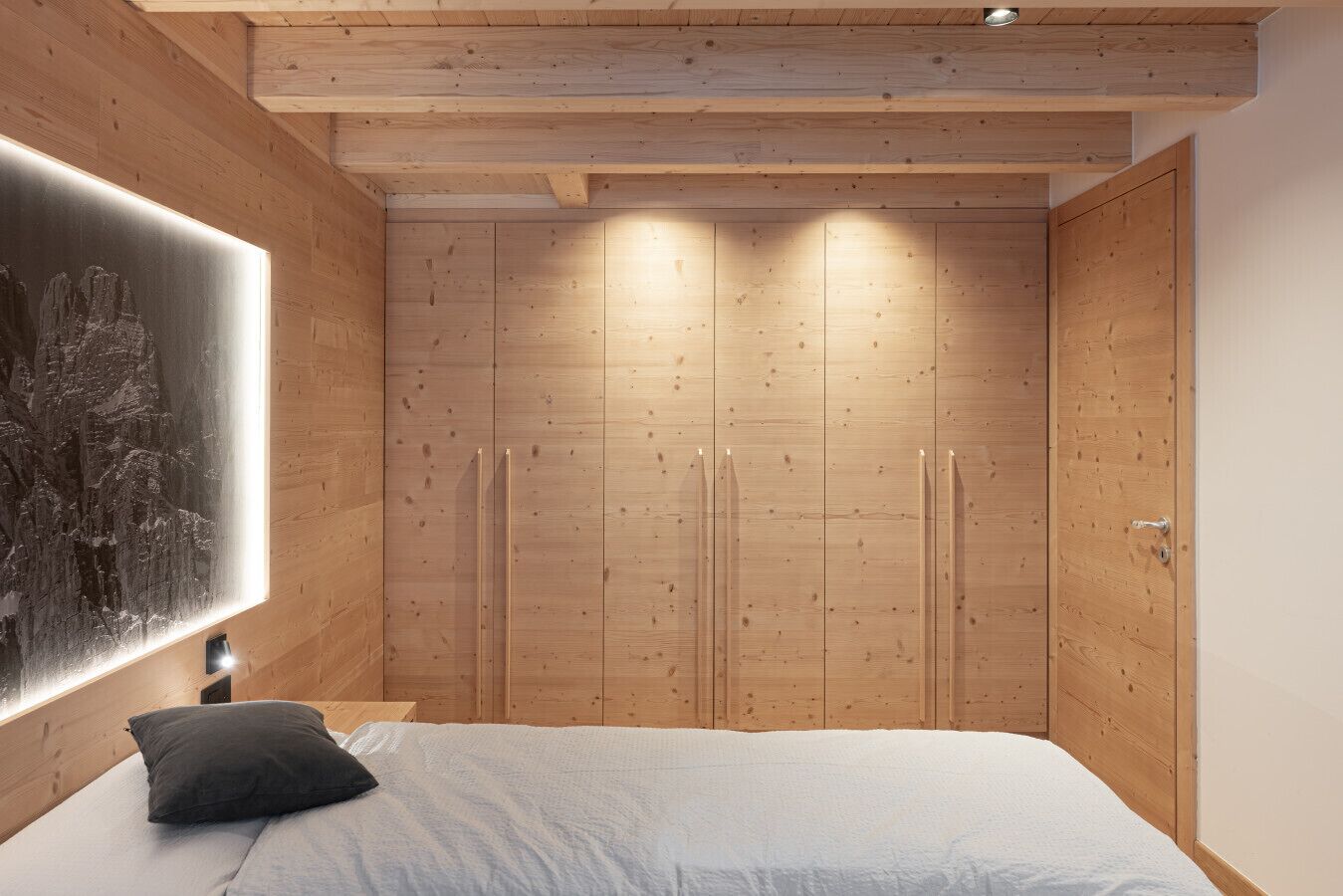 A bedroom with a bed, a wall-mounted light, and wooden cabinets.