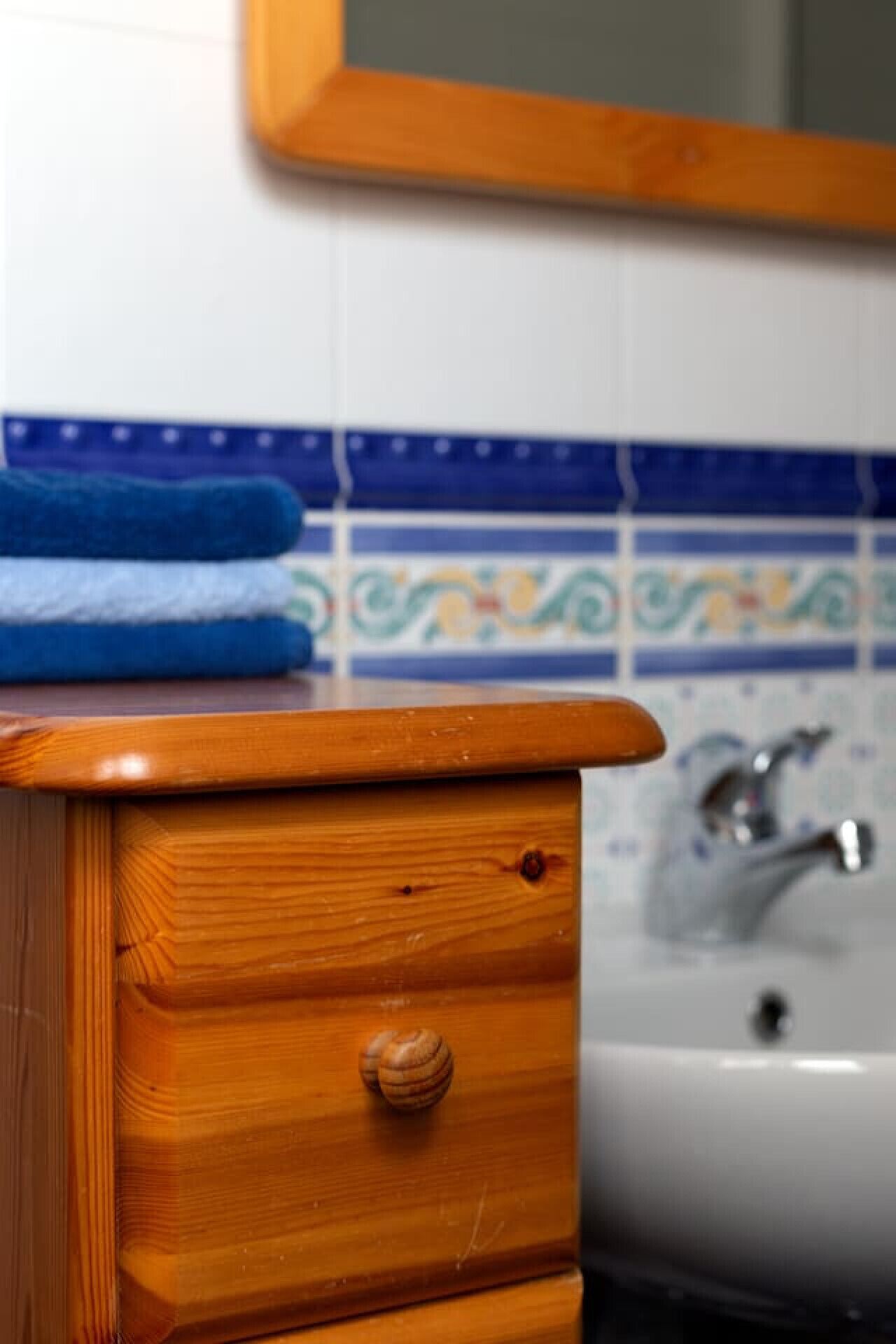 Un aparador de madera con un cajón y una pequeña perilla redonda, una toalla azul y un lavabo blanco con grifo.