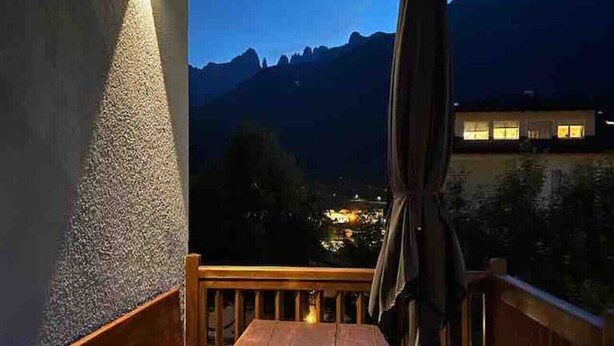 Een houten bank en tafel op een balkon met uitzicht op een berg bij zonsondergang.