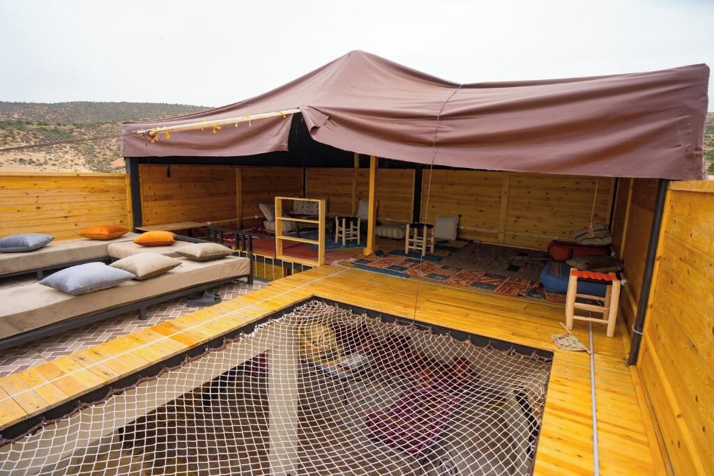 A wooden cabin with a covered outdoor seating area, a small table, and a netted pool.
