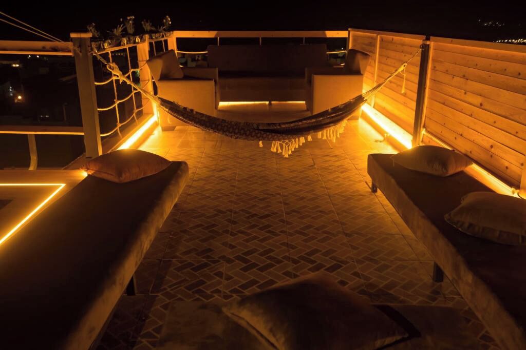 Eine Liege mit zwei Sitzgelegenheiten mit Polstern, einer Holzterrasse und Lichterketten.