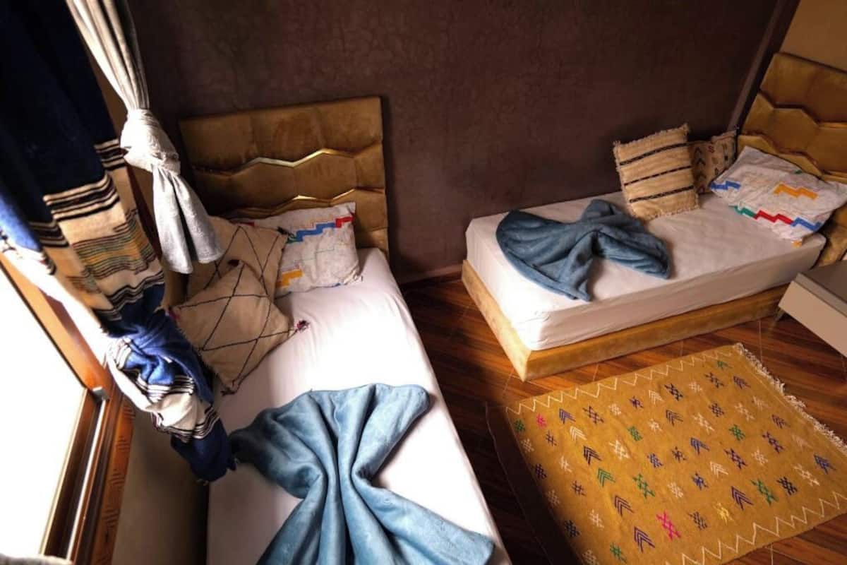 Una habitación con dos camas, una ventana con cortinas y una alfombra estampada.
