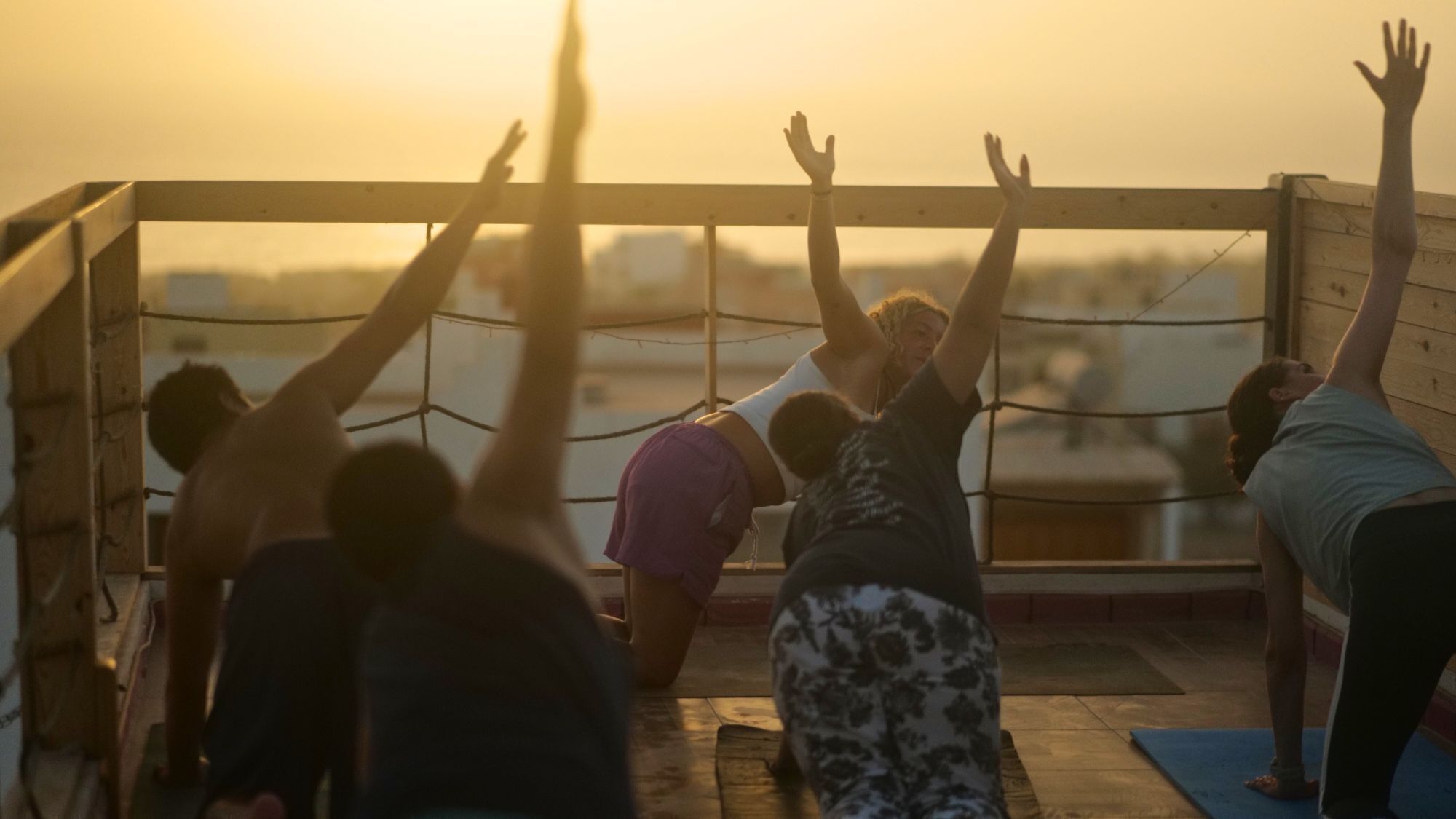 A group of people performing yoga on a wooden deck with a view of the sunset.