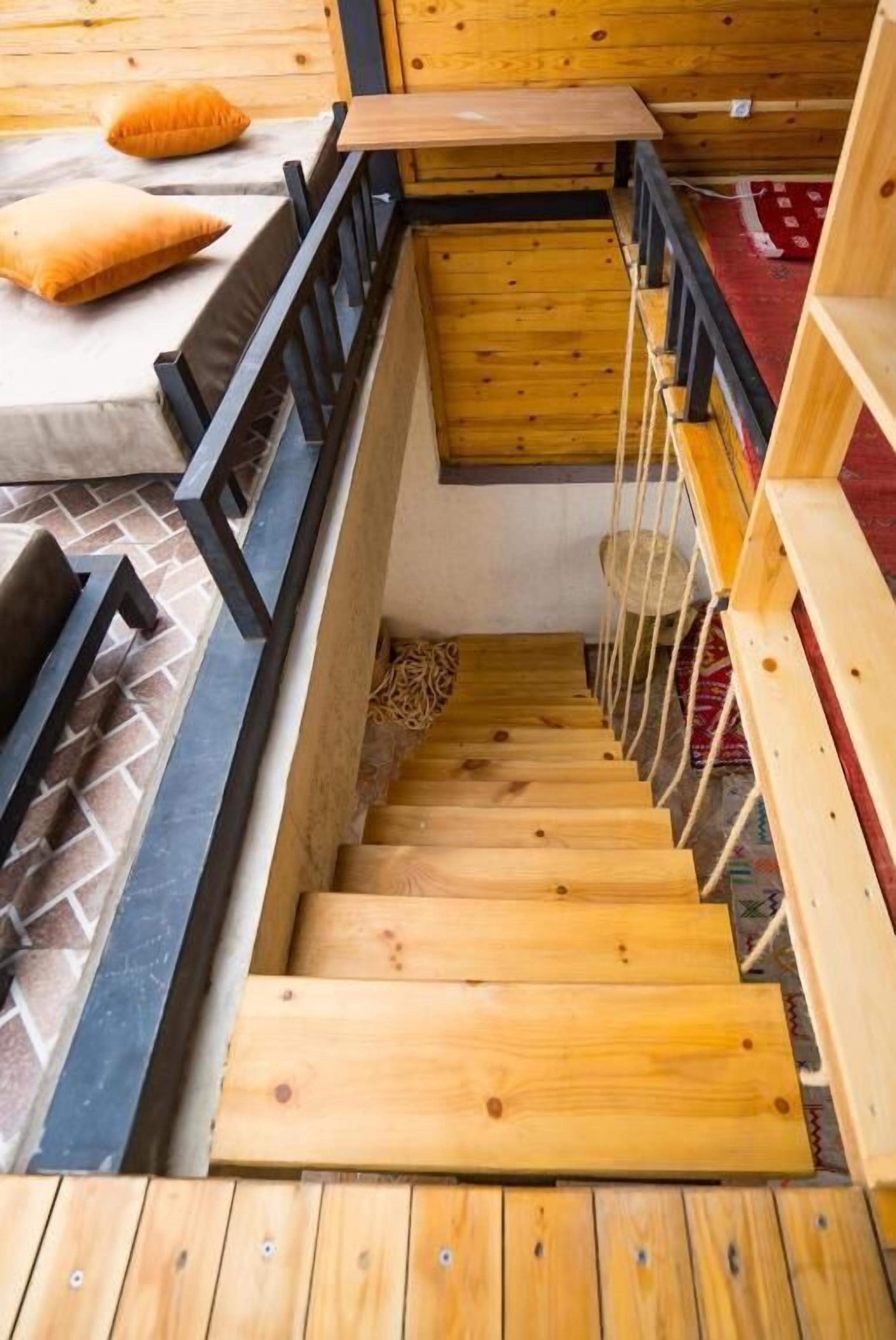 A wooden staircase with black railings leading to a bed area with a red carpet.