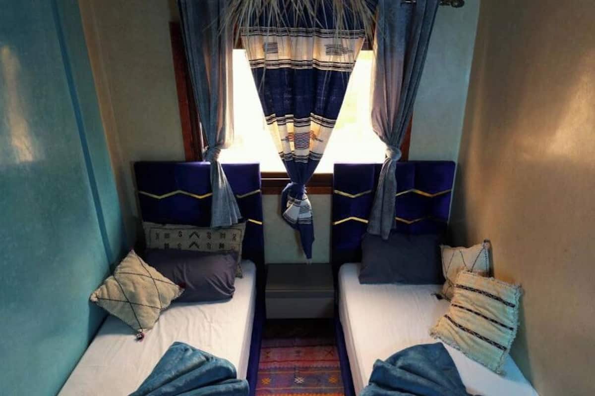 Un compartimento de tren estrecho con dos camas individuales, cada una con cabecero, almohadas y una mesita.