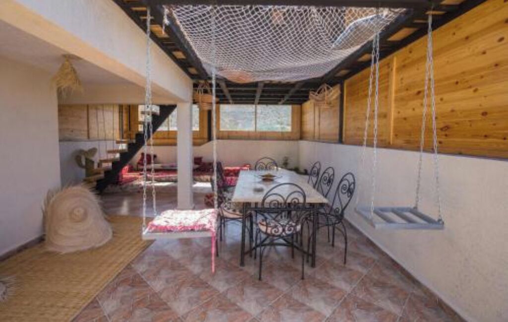 A dining area with a table and chairs, a hanging net, and a staircase in the background.