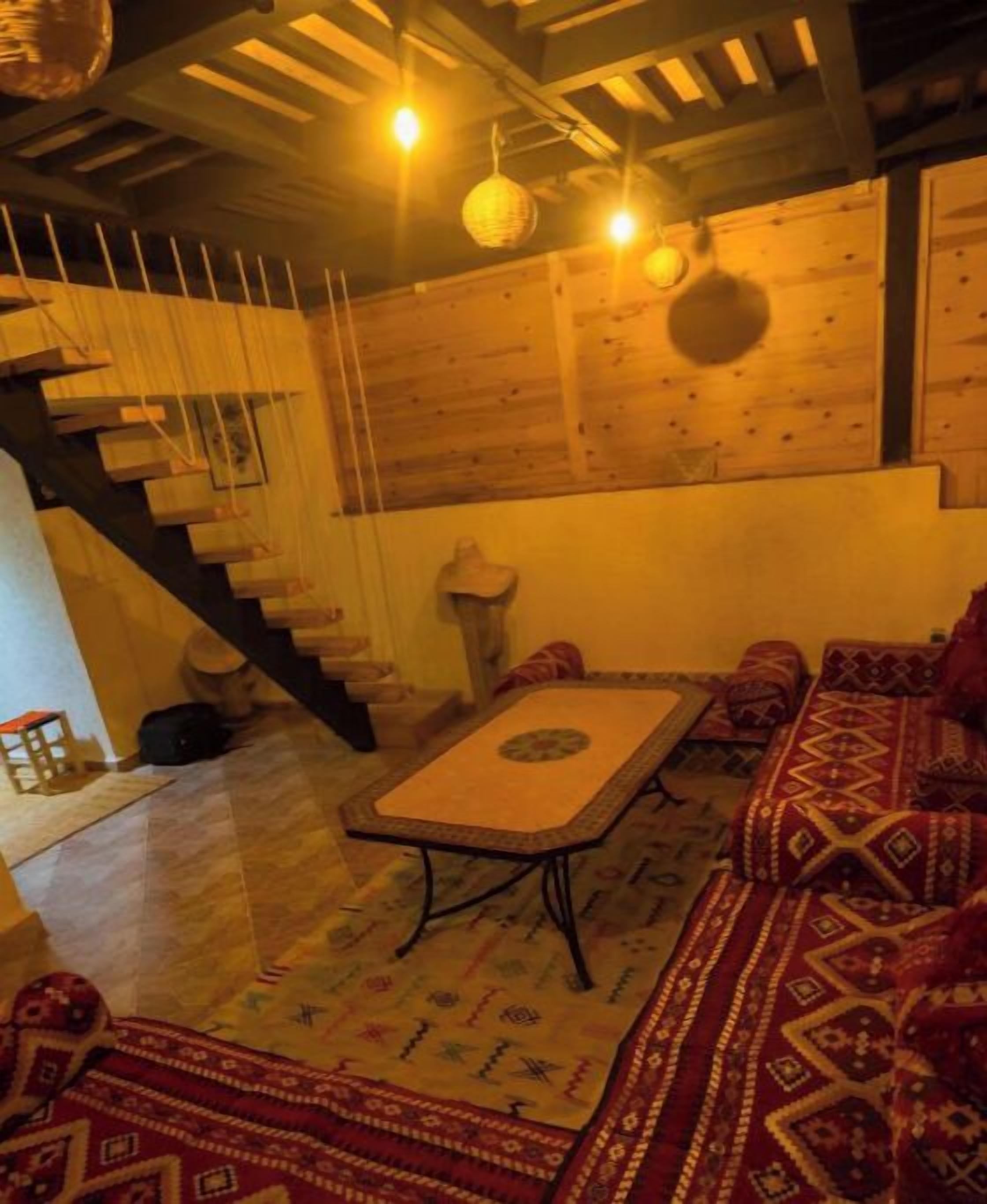 A cozy room with a wooden staircase, a patterned rug, and a sofa with red cushions.