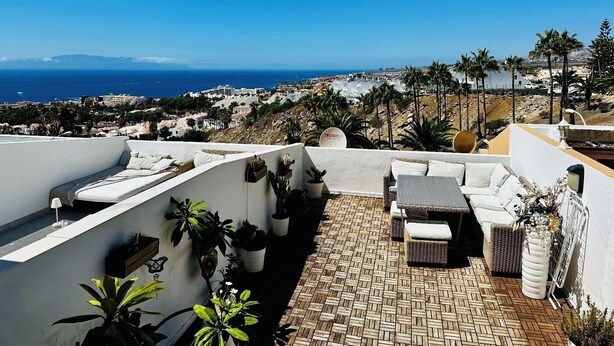 Une terrasse sur le toit offrant une vue sur la mer et le paysage urbain, aménagée avec des meubles d’extérieur et des plantes en pot.