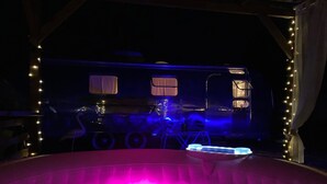 A hot tub with a pink hue, surrounded by string lights and a dark interior. - American caravan🇺🇸 with private SPA, near Beauval (Chabris)
