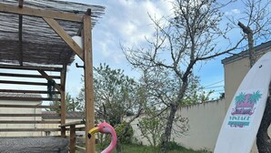 A wooden pergola with a patterned bench, a pink flamingo statue, and a surfboard leaning against a wall. - American caravan🇺🇸 with private SPA, near Beauval (Chabris)