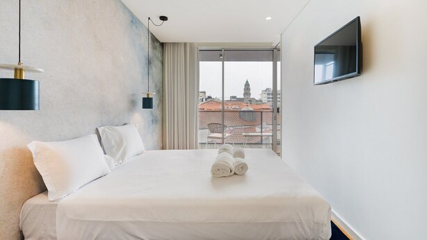 A hotel room with a large bed, a flat-screen TV, and a view of buildings through a large window.