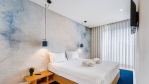 A modern hotel room with a large bed, bedside tables, a small plant, and a TV mounted on the wall.