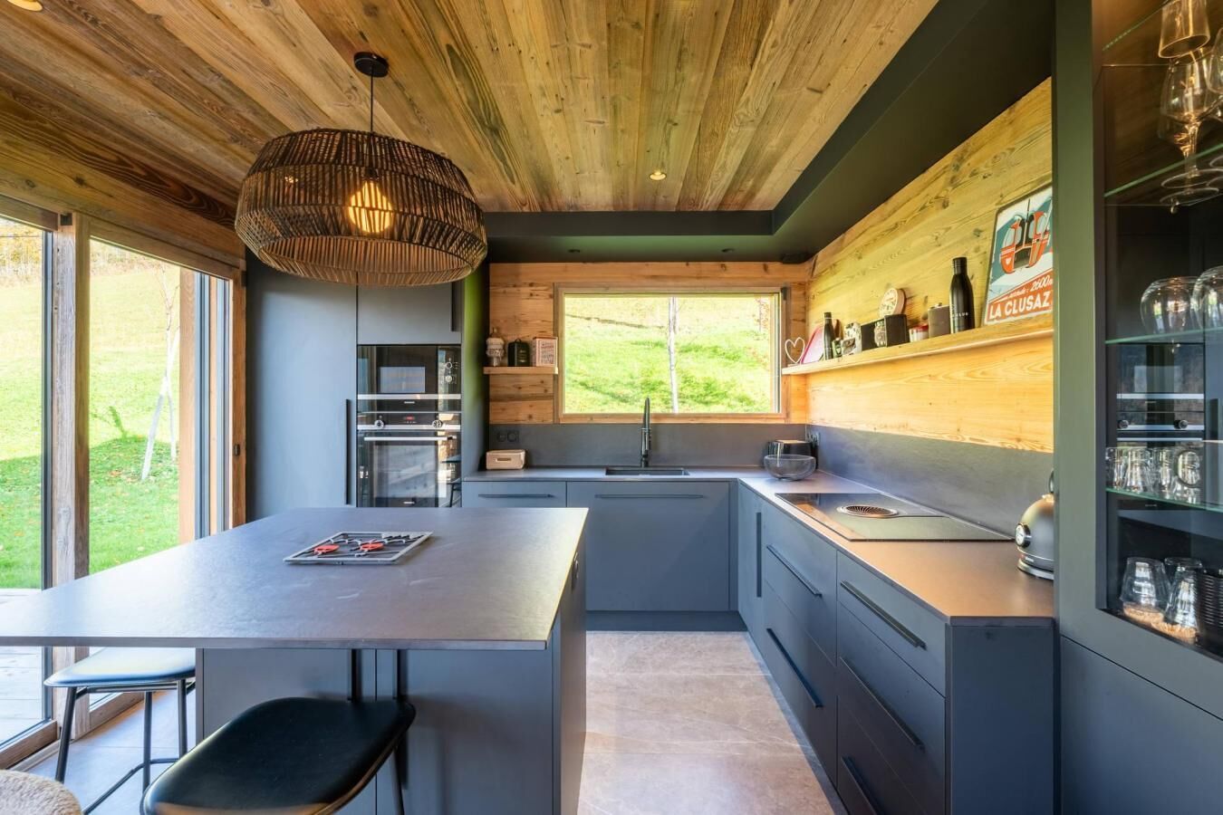 A modern kitchen with a large island, built-in oven, and a window overlooking a garden.