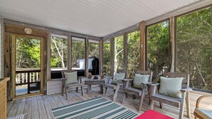 Eine überdachte Veranda mit Holzmöbeln, einer roten Bank und großen Fenstern mit Blick auf Bäume.