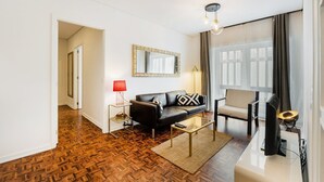 A modern living room with a black leather sofa, a red lamp, a glass coffee table, and a large mirror on the wall.