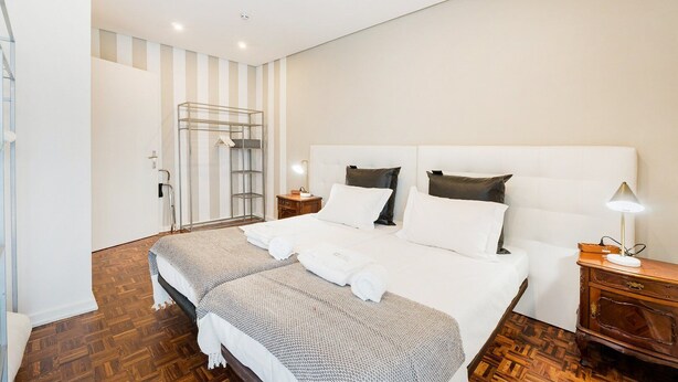A modern hotel room with a large bed, a wooden floor, a glass shower enclosure, and a bedside table with a lamp.