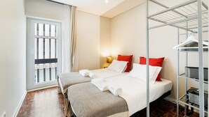 A hotel room with two beds, a wardrobe, a window with curtains, and a wooden floor.