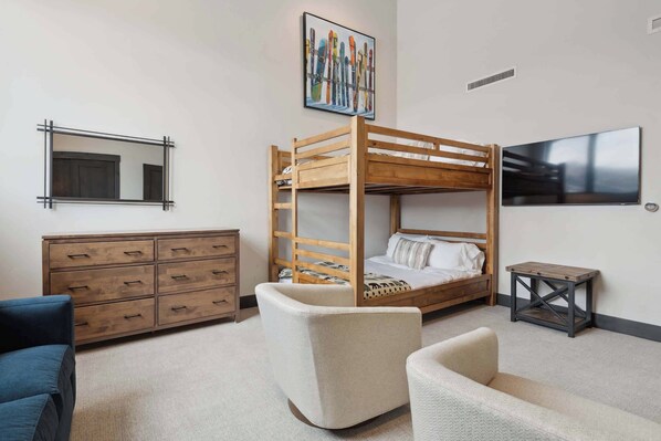 Un dormitorio con una cama individual, un aparador, una silla, una mesita, un televisor y un cuadro en la pared.