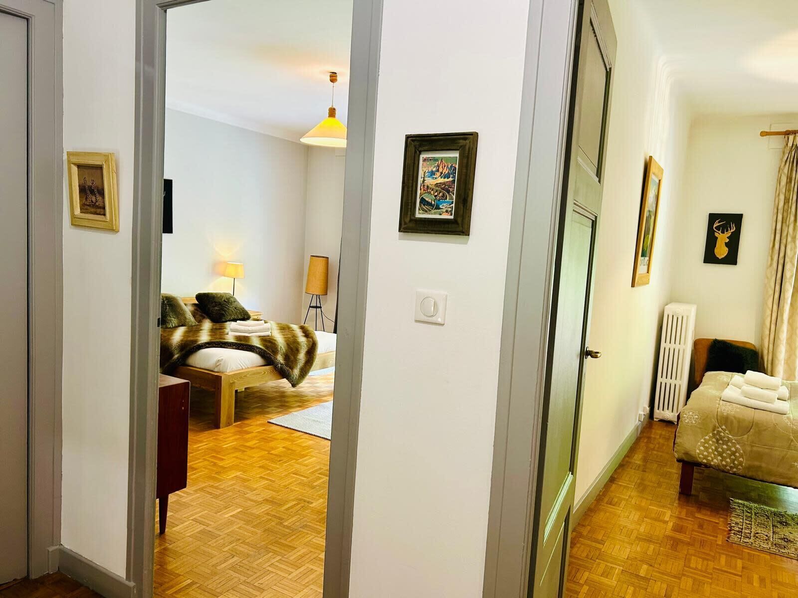 A hotel room with a wooden floor, a bed with a blanket, a bedside table with a lamp, and a radiator.