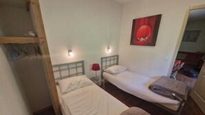 A small, compact room with two single beds, a wooden wardrobe, a red lamp, and a painting on the wall. - 200m from ski slopes, Ground floor, terrace, balcony, tv, ski locker, 45m², Valfréjus (Valfréjus)