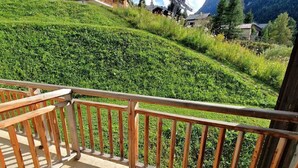A balcony with a wooden railing overlooking a green hillside with buildings in the background.