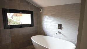 Une salle de bain moderne avec une baignoire sur pieds, une fenêtre et un mur à texture.