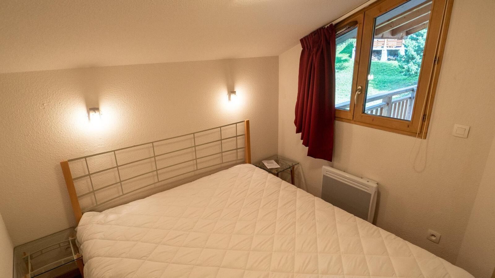 Un dormitorio con cama, mesita de noche y ventana con cortinas.