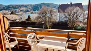 A wooden deck with a table and chairs overlooking a scenic view of a lake, houses, and hills.